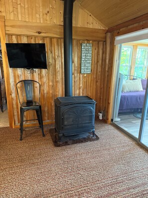 A cozy cabin interior with a wood-paneled wall, a black stove, a chair, and a television. - Cozy, Lakefront Cottage, 9 miles to Baxter, dock, kayaks, canoe, 2 bedroom (Millinocket)