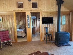 Interior acogedor de una cabaña con una cama, un sillón rojo, un televisor y un estufa de leña.