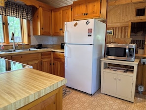 A kitchen with wooden cabinets, a white refrigerator, a microwave, and a sink. - Cozy, Lakefront Cottage, 9 miles to Baxter, dock, kayaks, canoe, 2 bedroom (Millinocket)