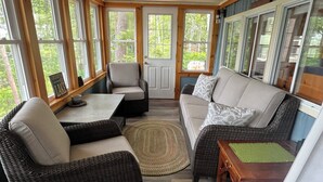 A sunroom with wicker furniture, a wooden table, and a view of the outdoors.