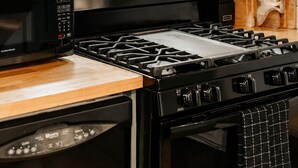 Eine Küche mit einem schwarzen Herd, einer Mikrowelle und einem Backofen, Holzregalen und einer gefliesten Spritzschutzleiste.