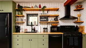 A kitchen with a black refrigerator, green cabinets, a microwave, a stove, and various kitchen utensils on shelves. - Rivers Ledge Cabin with Sauna and Hot Tub (Barrville)