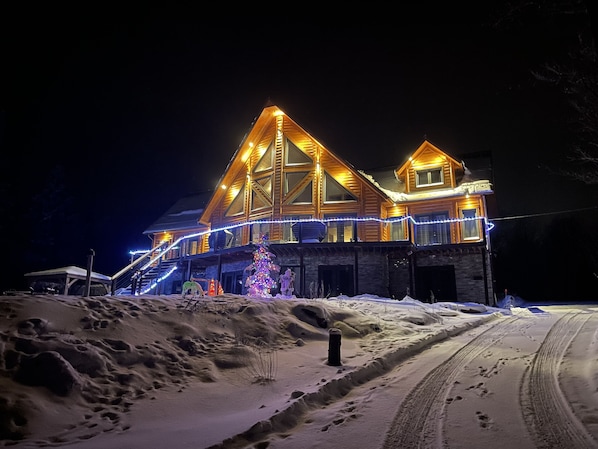 A two-story wooden cabin with a snow-covered driveway and a Christmas tree decorated with lights. - Family, Comfortable, Luxurious with Spa (Unit 2) (Saint-Joachim)