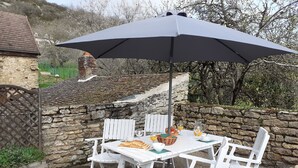 A patio with white chairs and a table set for breakfast, featuring bread, eggs, and juice.
