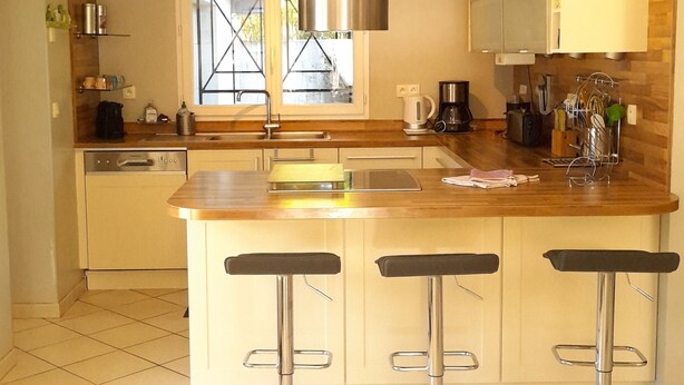 Een moderne keuken met een centraal kookeiland, roestvrijstalen apparatuur en barstoelen.