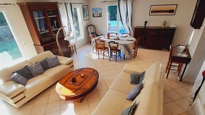 Een ruime woonkamer met een zithoek, een salontafel, en een eethoek met stoelen en een tafel.