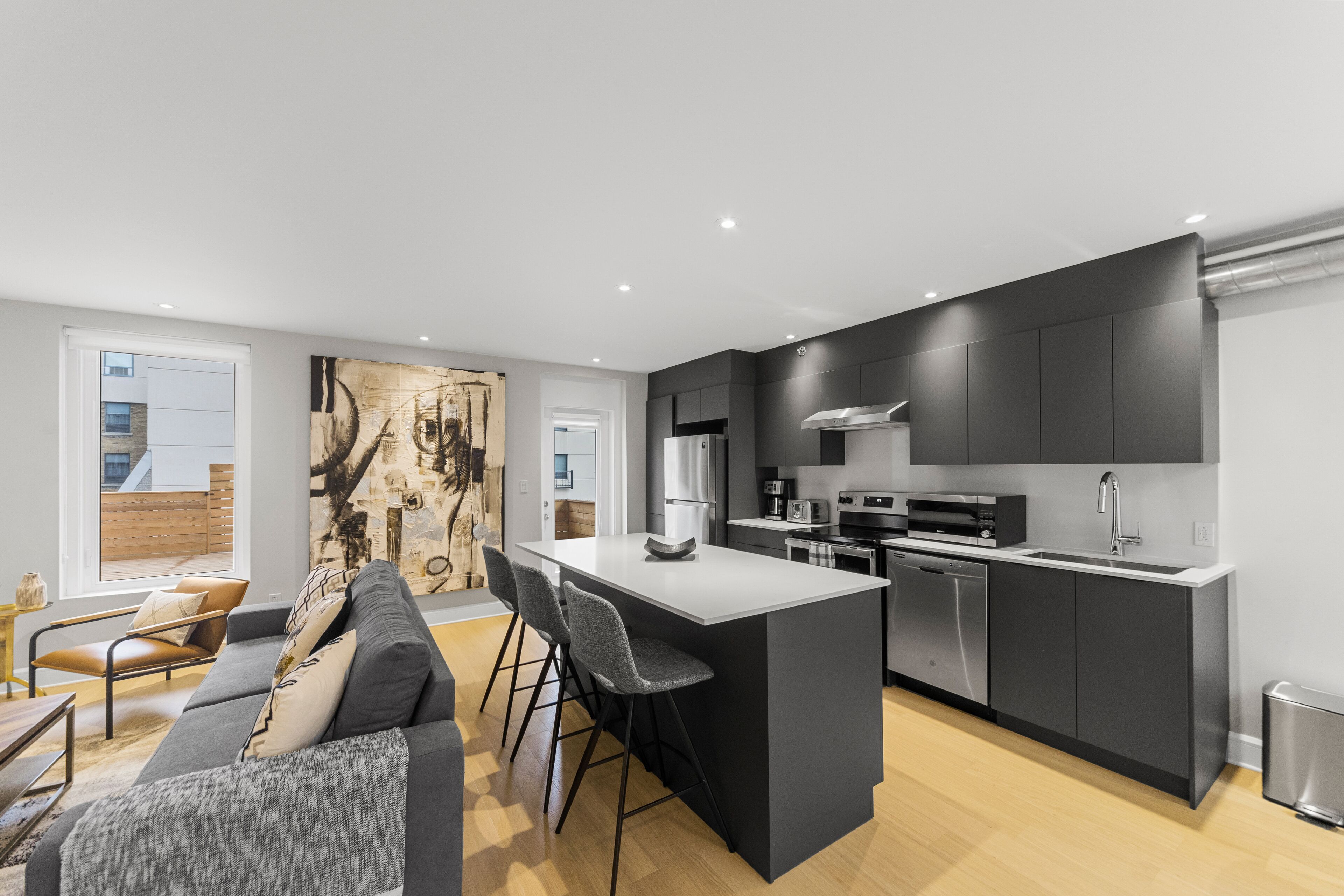 Una cocina moderna con una isla central, muebles oscuros y electrodomésticos de acero inoxidable.
