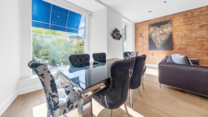 A modern living room with a glass dining table, black and white patterned chairs, a dark sofa, and a brick wall with a colorful artwork. - Elegant Suites De La Montagne- Dtwn Mtl (Montreal)