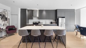 A modern kitchen with a central island, grey cabinets, and a dining area with bar stools. - Elegant Suites De La Montagne- Dtwn Mtl (Montreal)