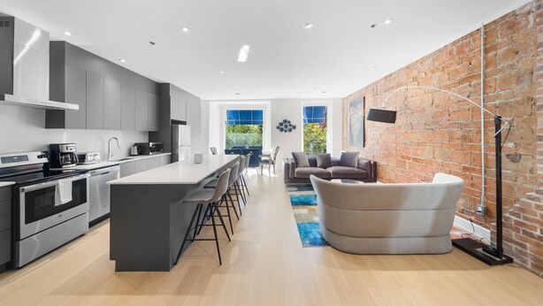 A modern kitchen with a central island, bar stools, and a dining area with a sofa and coffee table. - Elegant Suites De La Montagne- Dtwn Mtl (Montreal)