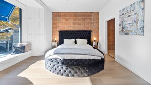 A modern bedroom with a round bed, a brick wall, and a large window. - Elegant Suites De La Montagne- Dtwn Mtl (Montreal)