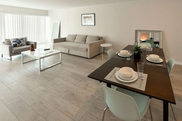 Una sala de estar moderna con comedor, que incluye un sofá, una mesa de centro y una mesa de comedor preparada para cuatro comensales.