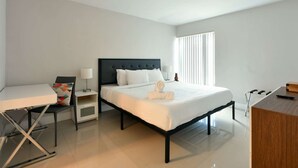 Una habitación de hotel con una cama, mesitas de noche, un escritorio y una ventana.
