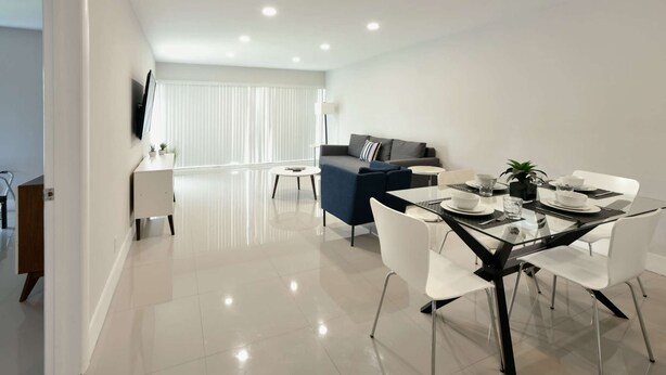 Una sala moderna con un sofá, una mesa de comedor para dos personas y un televisor montado en la pared.