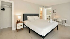 Una camera d'albergo con un letto, un comodino, una lampada e una scrivania con una sedia.