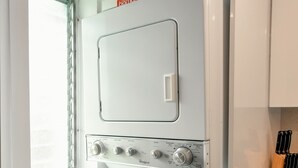 Una cucina compatta con lavatrice e asciugatrice integrate, un tagliere in legno e un portacoltelli.