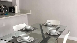 A modern dining area with a glass-top table, white chairs, and a kitchen counter in the background. - ✨Deluxe Designer Two Bedroom at Fort Lauderdale (Fort Lauderdale)