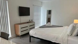 A modern hotel room with a bed, a desk, a dresser, a TV, and a mirror. - ✨Deluxe Designer Two Bedroom at Fort Lauderdale (Fort Lauderdale)