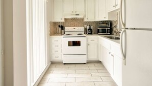 Une cuisine de taille réduite, avec des meubles blancs, une cuisinière, un four à micro-ondes et un réfrigérateur.