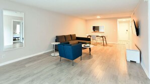 A modern living room with a sectional sofa, a blue armchair, a round coffee table, and a dining area with a table and chairs.