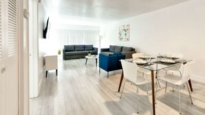 A modern living room with a sofa, a coffee table, and a dining area with a glass table and chairs. - ✨One Bedroom Stunning River Views at Fort Lauderdale (Fort Lauderdale)
