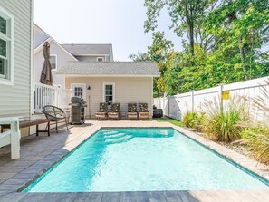 A rectangular swimming pool with a wooden deck, surrounded by a white fence and a house in the background.
