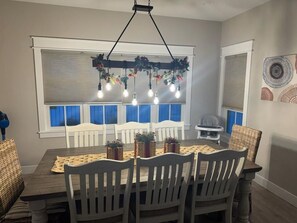 A dining area with a wooden table, white chairs, and a hanging light fixture with multiple bulbs.