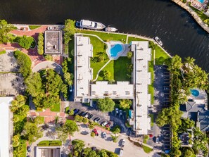 An aerial view of a hotel with a swimming pool, parking area, and a waterfront location.