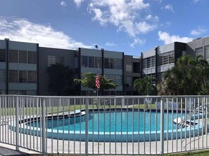 A swimming pool surrounded by a white fence, with a building in the background.