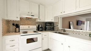 A kitchen with white cabinets, a stove, a microwave, and a coffee maker. - ✨Brand New Designer Two Bedroom Apartment at Fort Lauderdale (Fort Lauderdale)