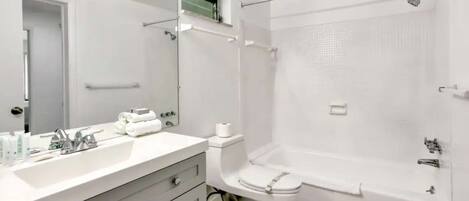 Un baño moderno con un espejo grande, un lavamanos con artículos de aseo, un inodoro y una ducha a ras de suelo.