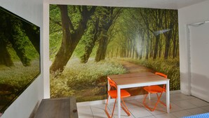 Une pièce dont un mur est orné d’une grande fresque représentant une forêt, avec une table en bois et des chaises orange.