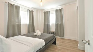 A bedroom with a bed, grey curtains, a small table, and a light fixture. - ✨ One Bedroom Chic and Cool - Large (Full Kitchen) (Miami)