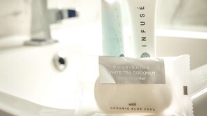 Une salle de bain avec un lavabo blanc, une bouteille blanche étiquetée « THÉ BLANC NOURRISSANT À LA NOIX DE COCO » et un savon.