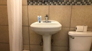 Casa de banho com lavatório pedestal branco, sanita e caixote de lixo.