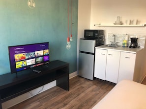 A compact kitchenette with a microwave, refrigerator, and a small sink. A flat-screen TV is mounted on a dark wooden console table.
