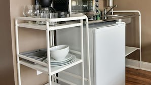 Un chariot de cuisine blanc, doté d’étagères où sont rangés des bols et des verres, ainsi qu’un grille-pain et une bouilloire.