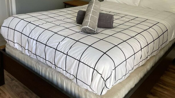 A neatly made bed with a white and black checkered bedspread, two pillows, and a wooden nightstand beside it. - ✨New, Trendy, Cool Wynwood Flat-12 (Miami)