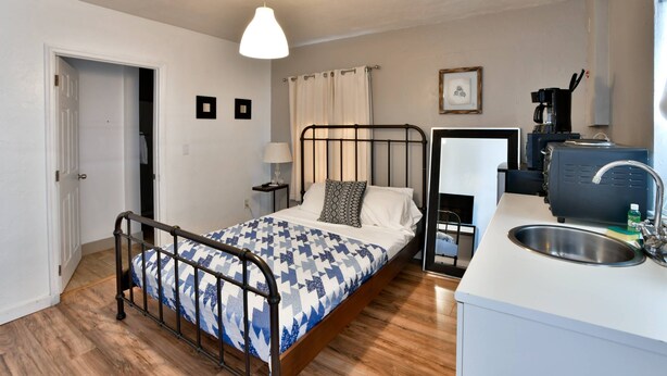 A compact bedroom with a bed, bedside table, lamp, and a small kitchenette with a sink and coffee machine. - ✨One Bedroom Chic and Cool (Miami)