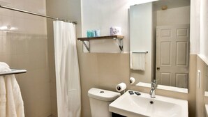 A bathroom with a toilet, sink, and shower curtain. There is a shelf above the toilet with toiletries. - ✨One Bedroom Chic and Cool (Miami)