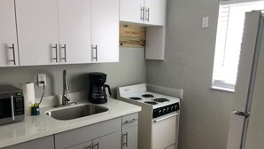 A compact kitchen with white cabinets, a stainless steel sink, a stove, and a coffee maker.