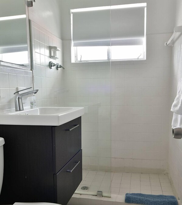 A bathroom with a white sink, dark cabinet, and a window above the shower.