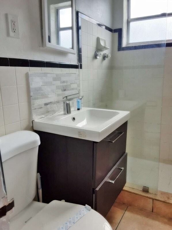 A bathroom with a white sink, dark cabinets, a toilet, and a glass shower enclosure.