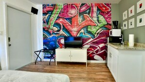 A room with a colorful graffiti wall, a television, a white cabinet, and a wooden floor. - ✨Bright amazing studio in Wynwood (Miami)