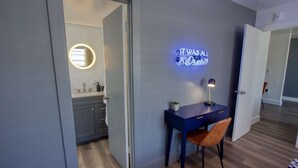 Een moderne slaapkamer met een bureau, stoel en een neonbord aan de muur.