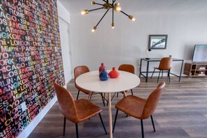 Une pièce moderne avec une table ronde, des chaises marron, un mur coloré orné de noms de villes, un luminaire suspendu et un tableau encadré accroché au mur.