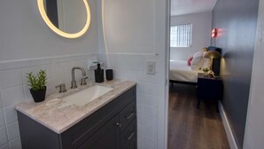 Un baño moderno con lavamanos de mármol, un espejo redondo y una planta en maceta.