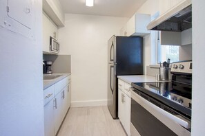 Una cocina moderna con electrodomésticos de acero inoxidable, armarios blancos y un ventanal que proporciona luz natural.
