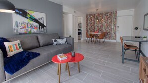 A modern living room with a grey sofa, a red coffee table, and a cityscape painting. - Amazing Renovated One Bedroom w/Free Parking and Pool with Balcony (Miami)