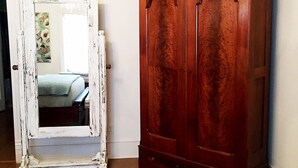 A room with a wooden wardrobe and a white-framed mirror leaning against the wall. - Marie Celeste Creole Country Cottage (Destrehan)